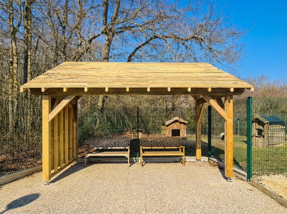 Photographie d'une charpente bois artisanale de style traditionnel, fraîchement réalisée, en cours de finition ou récemment achevée. La structure doit montrer clairement une ossature bois massif et bien travaillé, idéalement une couverture ou un auvent en bois protégeant une terrasse, un carport ou un espace extérieur. Les détails d'assemblage du bois (tenons, mortaises, jointes) doivent être visibles, témoignant du travail artisanal de qualité. L'image doit être prise en extérieur en plein jour, mettant en évidence l'esthétique et la solidité de la structure bois, avec un environnement résidentiel en arrière-plan pour contextualiser l'utilisation à titre privé.