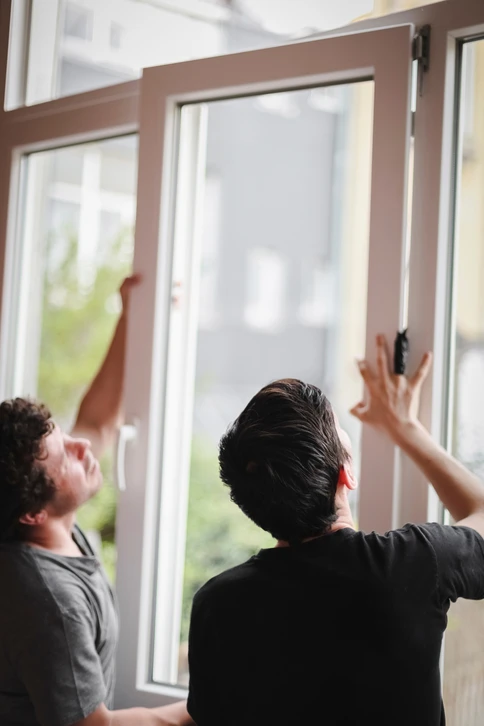 Deux ouvriers installent une fenêtre à battant en bois dans une construction neuve aux murs en lambris